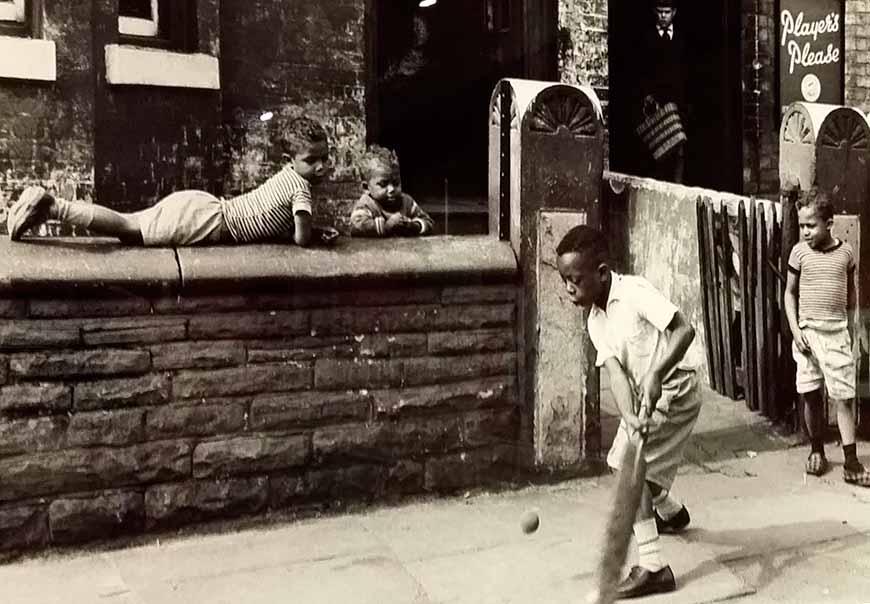 Young black boys play cricket on the pavement (Негритёнок, играющий в крикет на тротуаре)