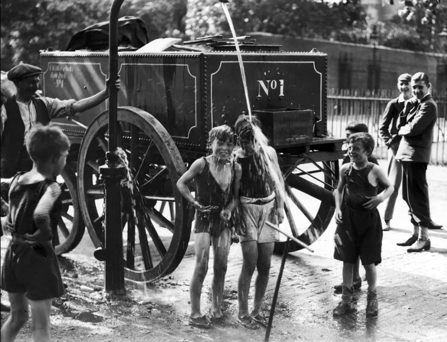A water cart man turns the water main on a group of boys to help them cool off during a heatwave (Водовоз направляет кран на группу мальчиков, помогая им охладиться во время сильной жары), 1930