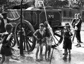 A water cart man turns the water main on a group of boys / Водовоз направляет кран на группу мальчиков