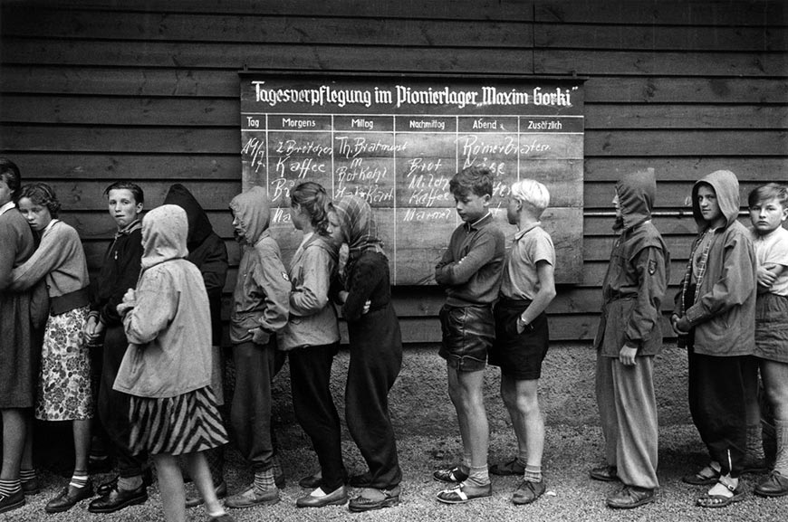 East German youth members of the 'Maxim Gorki Pionierlager' waiting for meal distribution, panel shows daily food rations (Восточногерманские пионеры из пионерлагеря "Максим Горький" в ожидании обеда, табло демонстрирует ежедневные рационы питания), 1957