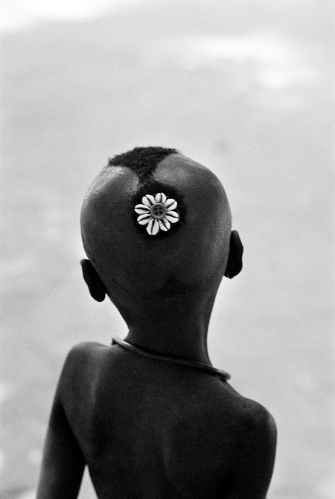 Young Diola boy with shells woven into his hair watching warriors during their dances (Мальчик племени Diola, с вплетёнными в волосы ракушками, наблюдает за воинами во время их танцев) 