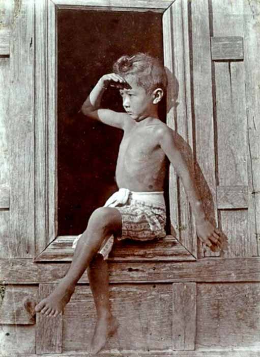 A young half-dresssed thai boy looking at the horizon, sitting on a wooden window sill (Юный полуодетый тайский мальчик смотрит на горизонт, сидя на деревянном подоконнике), c.1900 Siam