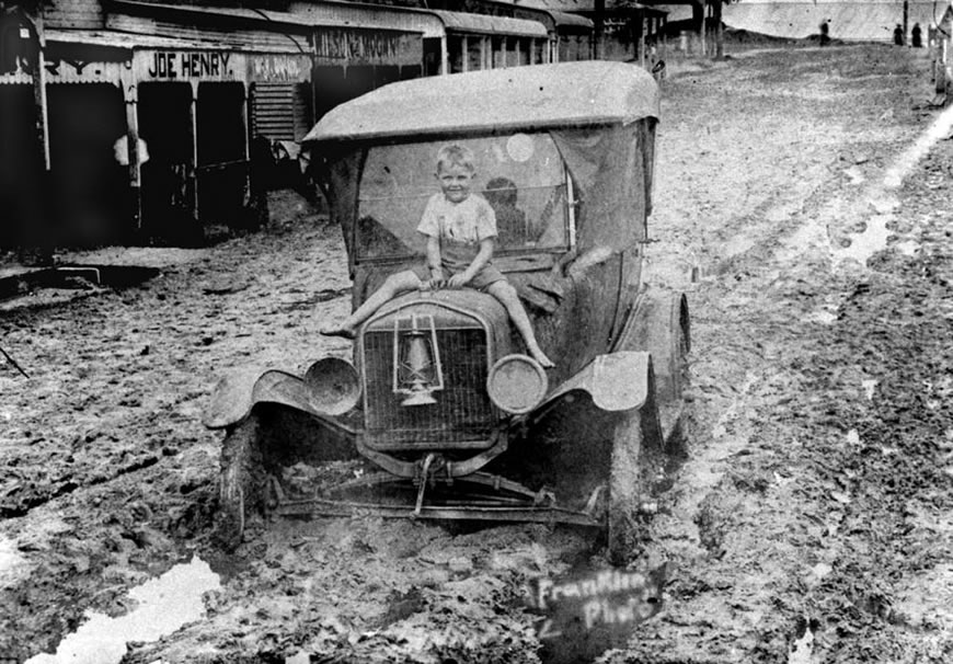 Boy sitting on the bonnet of a car bogged in mud from the flood (Мальчик сидит на капоте машины, застрявшей в грязи наводнения), 1925