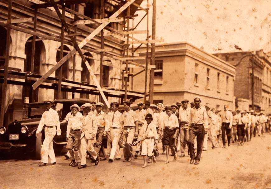 Dozens of boys, part of the Honolulu Police Department’s Junior Police Officers, parade down a street (Мальчики, часть Юных Полицейских полицейского департамента Гонолулу, участвуют в параде), 1920s