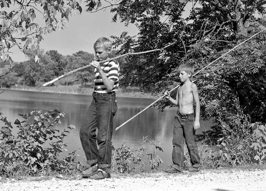 Two boys walk down path at Milan Reservoir with long fishing rods over their shoulders (Два мальчика идут по тропинке в Миланском водохранилище с длинными удочками на плечах), c.1955