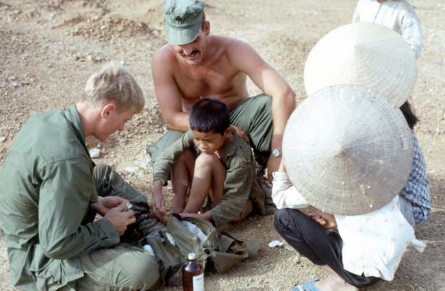 A U.S. Marine filling in for an absent Navy corpsman and treating the minor sores of a village boy (Морской пехотинец США заменяет отсутствующего санитара и лечит небольшие язвы деревенского мальчика), 1967 