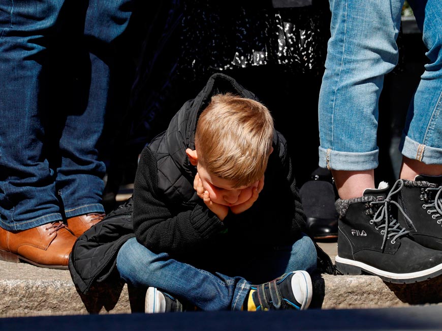 A boy sits on the ground during a minute's silence outside Windsor Castle on the day of the funeral of Britain's Prince Philip (Мальчик, сидящий на земле во время минуты молчания снаружи Винзорского замка в день похорон британского принца Филиппа), April 2021