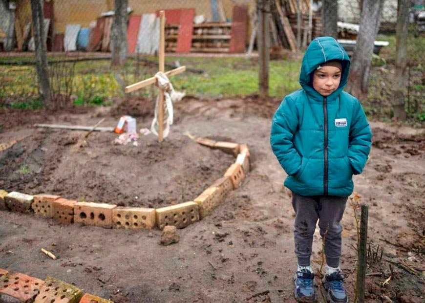 A boy [6] near the grave of his murdered mother whom they were forced to bury right in the backyard (Мальчик [6] возле могилы убитой матери, похороненной во дворе дома), April 2022