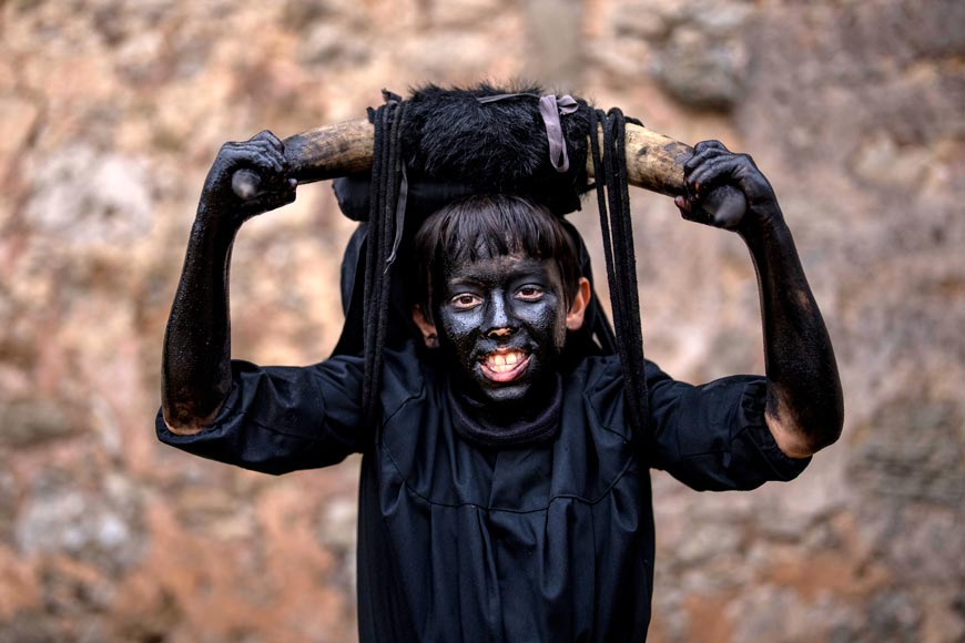 A reveler, dressed as 'Diablos de Luzon' or Luzon Devil's, covered in oil and soot carrying bull horns on his heads and cowbells on belts representing the devil (Участник карнавала, одетый как «Дьявол из Лусона», покрытый маслом и сажей, с бычьими рогами на голове и колокольчиками на ремнях, изображающий дьявола), Feb.2022