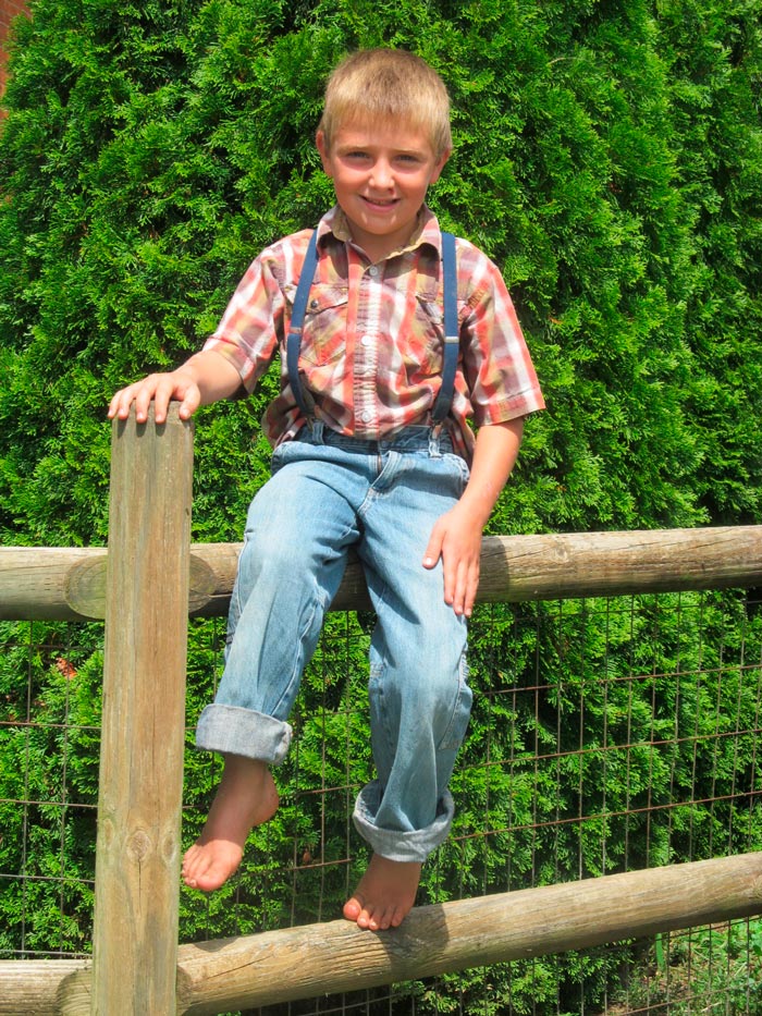 Mennonite boy sits on a fence in front of his farm house (Мальчик-меннонит, сидящий на заборе перед своим домом), 2014