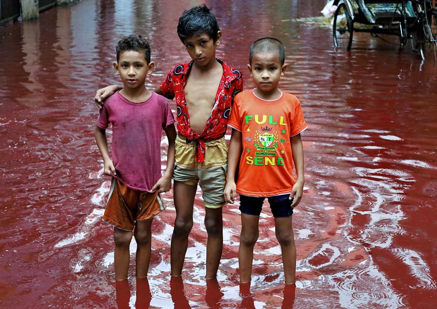 Three boys stand in a street flooded from heavy rain mixed with the blood of animals slaughtered for Eid Ul Adha (Три мальчика стоят на улице, залитой проливным дождем, смешанным с кровью животных, забитых на Курбан-Байрам), 2023