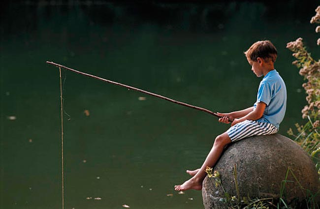 Boy sitting on rock by lake, fishing (Рыбачущий мальчик, сидящий на камне у озера)