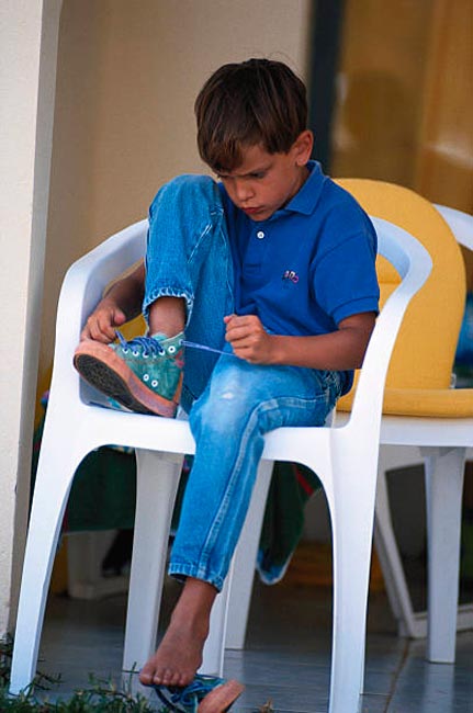 Boy on chair tying shoelace (Мальчик в кресле, зашнуровывающий убувь)