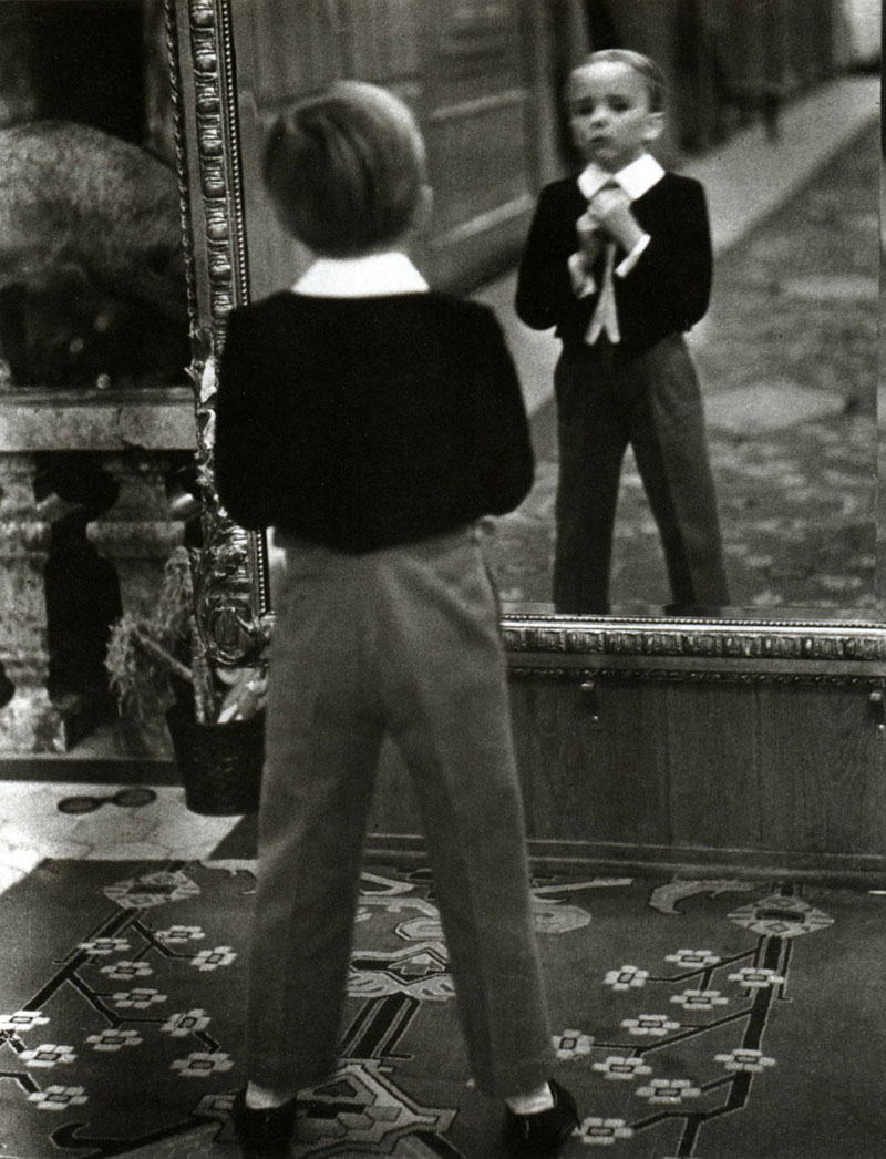 A small boy adjusts his tie before the impressive mirror in the foyer of the Grand Hotel, Saint-Moritz, Switzerland, 1932