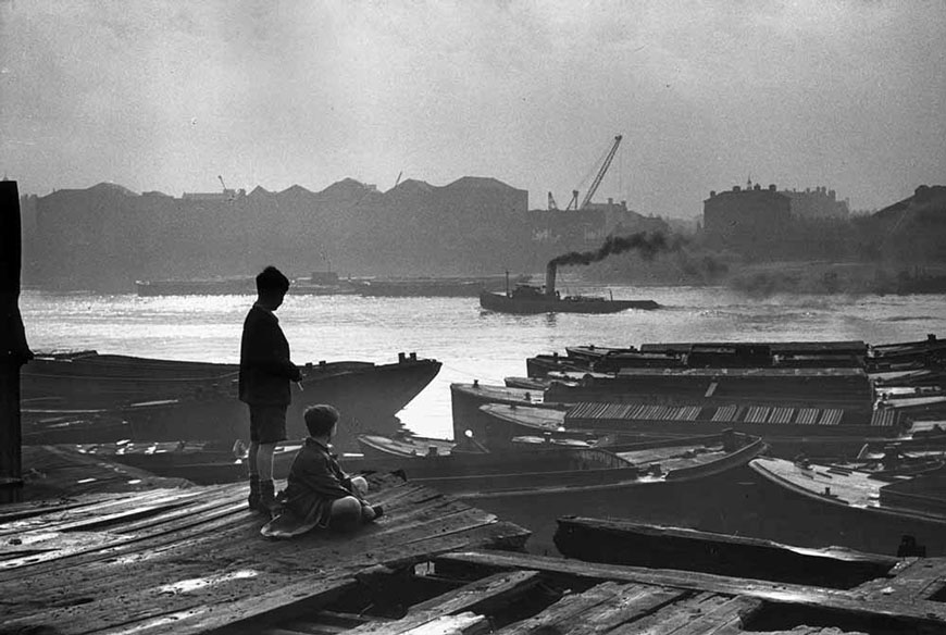 Boys from Wapping watch from an old wooden dock as a tug boat steams past on the Thames (Мальчики из Ваппинга наблюдают со старого деревянного причала за проплывающим по Темзе буксиром), 10 December 1949