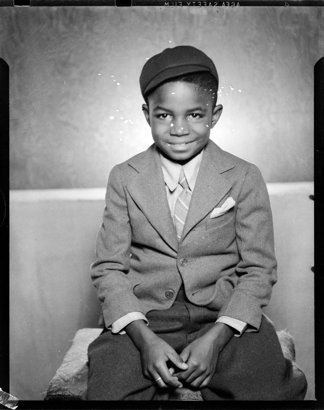 Portrait of boy wearing suit jacket, striped tie, and dark cap, seated on bench in Harris Studio (Портрет мальчика в пиджаке, полосатом галстуке и темной кепке, сидящего на скамейке в студии Харриса), c.1944