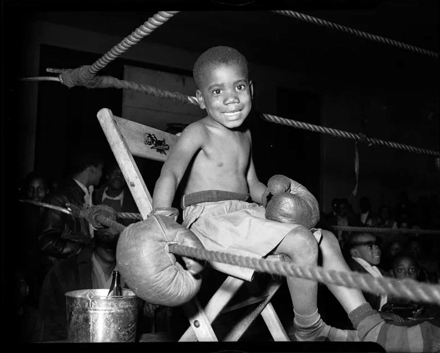 Little boy boxer, seated in boxing ring, possibly in Kay Boys' Club (Маленький мальчик-боксер, сидящий на боксерском ринге, возможно, в клубе Кэй Бойз), c.1945