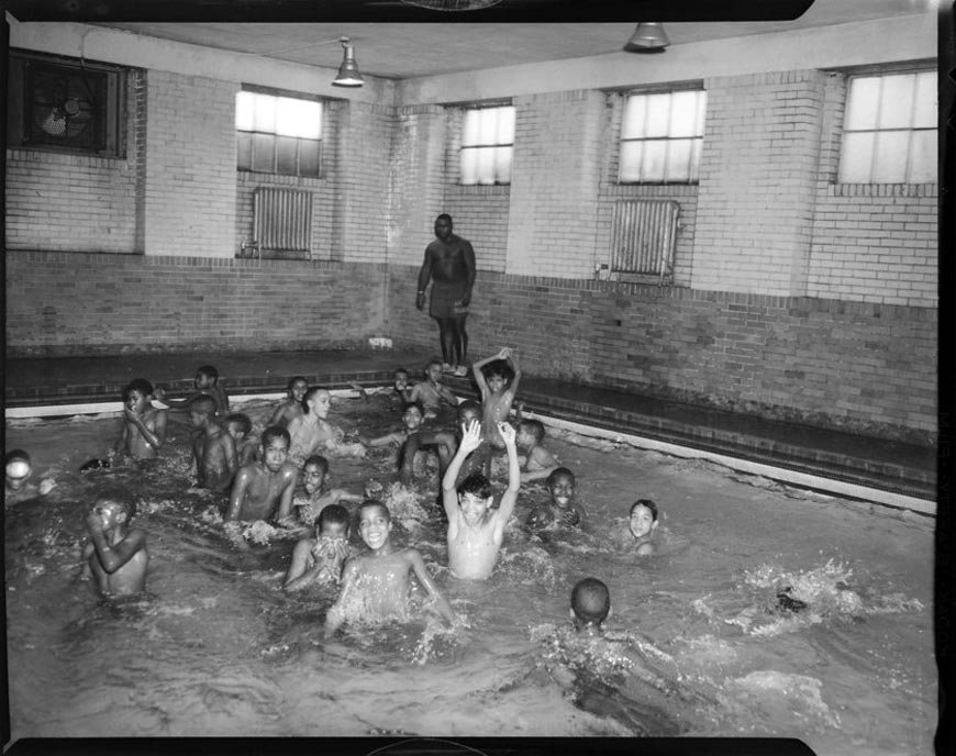 Boys splashing in indoor swimming pool, with man wearing swimming trunks inscribed 'head guard' standing in background, possibly in Centre Avenue YMCA (Мальчики плещутся в крытом бассейне, а на заднем плане стоит мужчина в плавках с надписью «главный охранник», возможно, в ИМКА на Центральном проспекте), c.1959