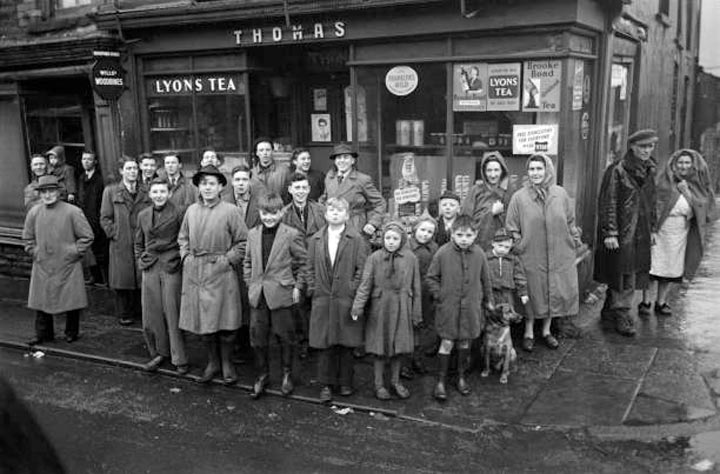 A crowd of people including children gather outside a general store in the rain to support a miners' strike (Толпа людей, включая детей, собравшаяся возле магазина под дождем, чтобы поддержать забастовку шахтеров), 1952