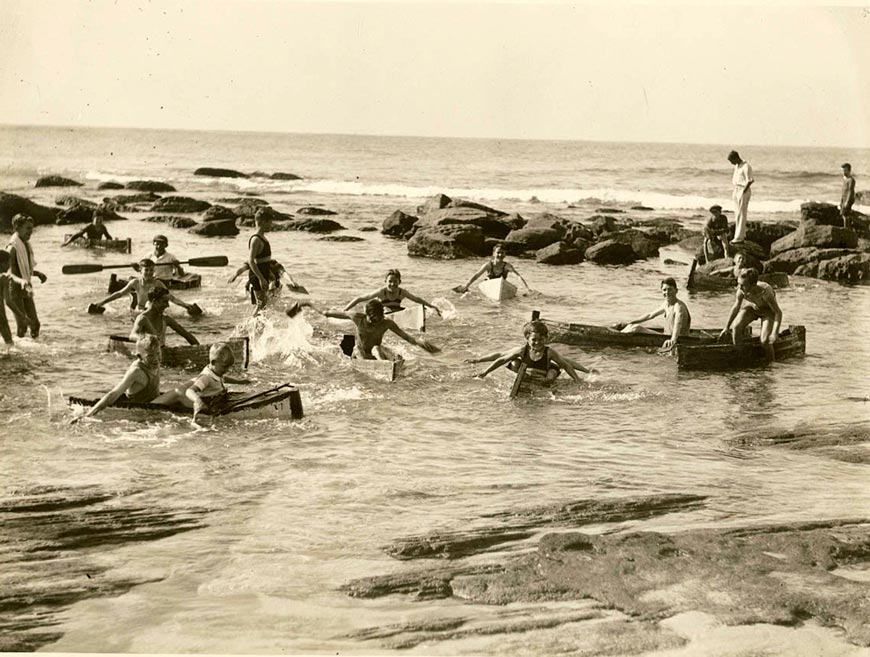 Men and boys swim and play in canoes in a beach rock pool (Мужчины и мальчики плавают и играют на каноэ среди прибрежных скал)