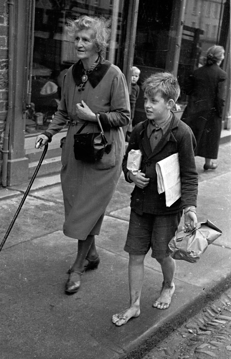 Lady Maud Montgomery and barefoot young boy helps her with her purchases, out shopping (Леди Мод Монтгомери и босоногий мальчик, помогающий ей с покупками после похода по магазинам), October 1943 Moville, Ireland