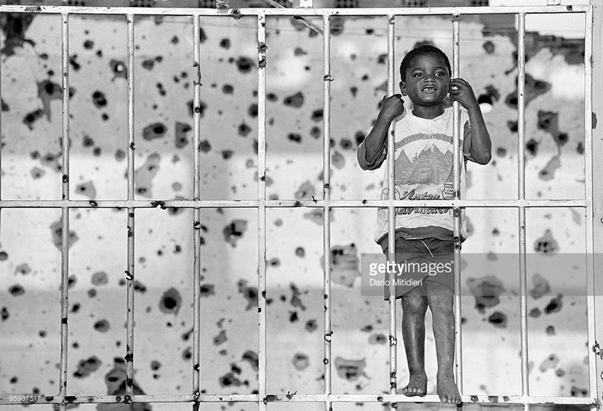 A child playing in front of a devastated bullet ridden wall (Ребёнок, играющий перед испещрёной пулями стеной), 1997