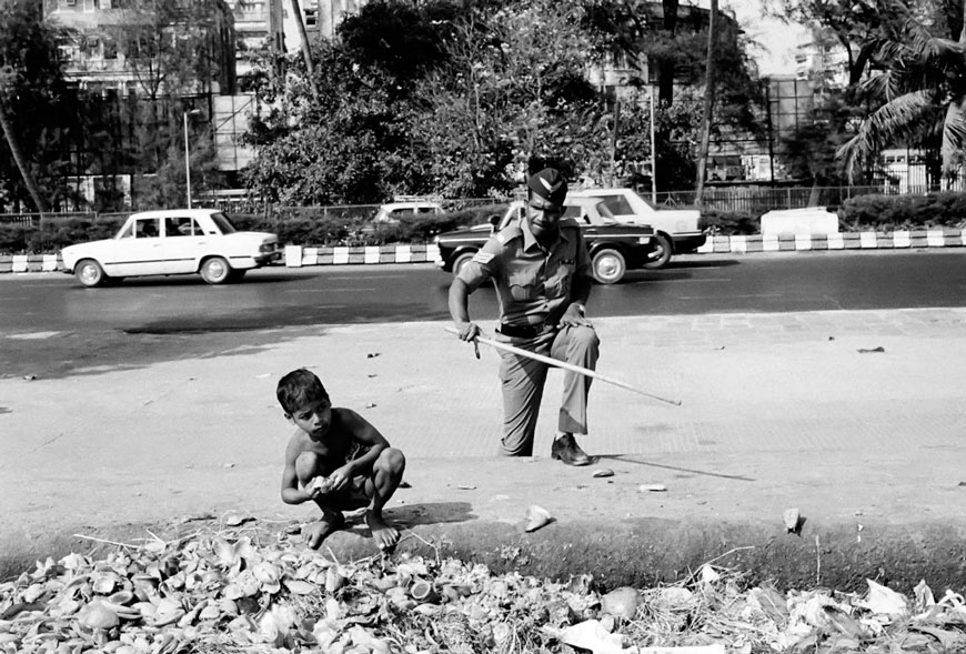 A street child who is searching for food at Chowpatti beach on Easter day is about to be beaten by a policeman