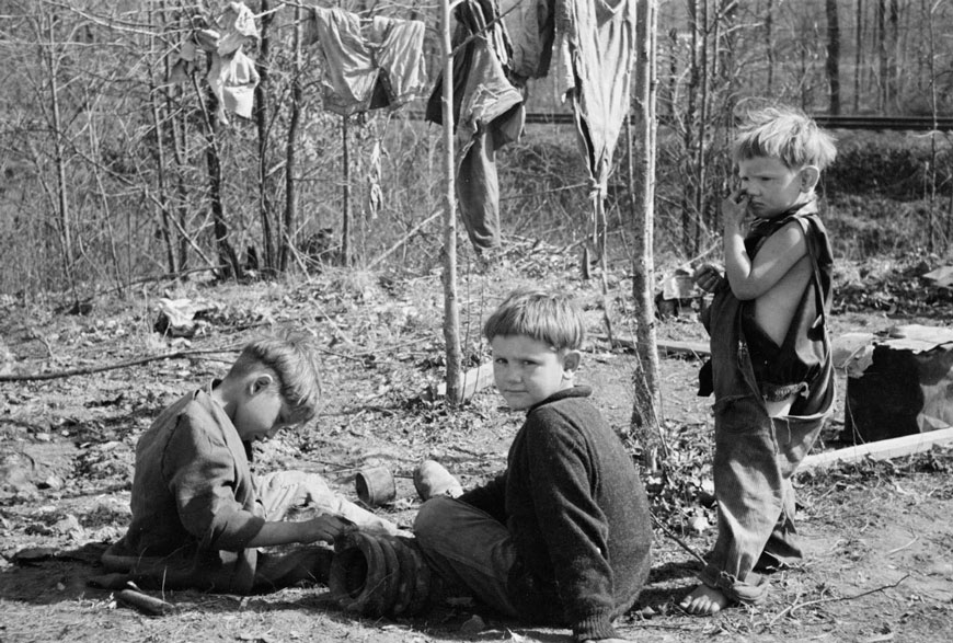 Three of the family of nine living in field in rough board covering built on old Ford truck chassis on U.S. Route 70, March 1936