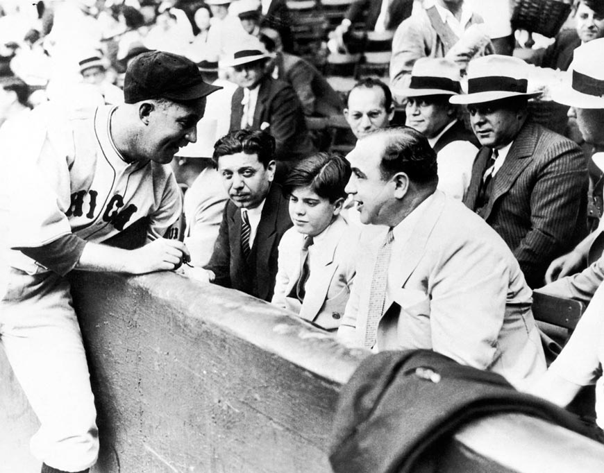 Chicago Cubs player Gabby Hartnett autographs a baseball for Sonny Capone who sits with his father Al Capone and other gangsters at a charity baseball game (Игрок «Чикаго Кабс» Гэбби Хартнетт даёт автограф Сонни Капоне, сидящем рядом со своим отцом Аль Капоне и другими гангстерами на благотворительном бейсбольном матче), 1931