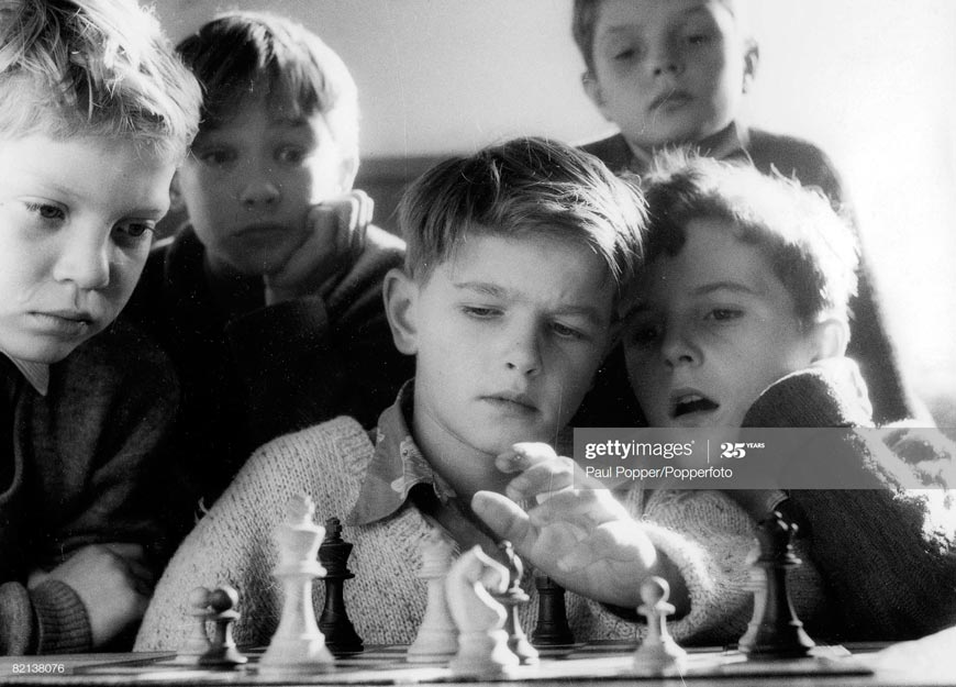 A group of young boys play a game of chess (Группа мальчиков, играющих в шахматы)