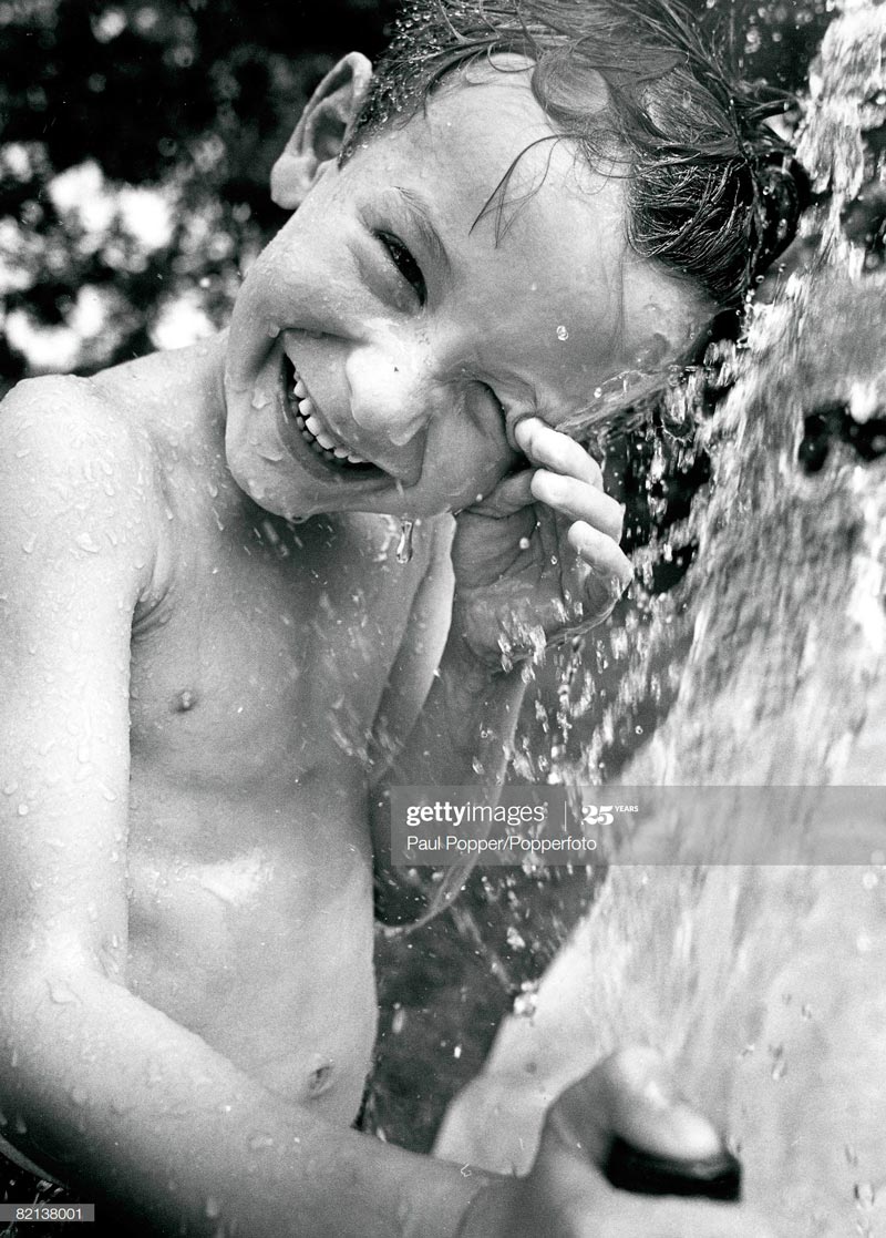 A young boy laughing as he plays under a spray of water (Смеющийся мальчик, играющий под струёй воды)