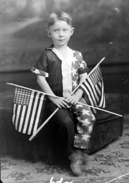 Young boy in patriotic attire holding two American flags (Мальчик в патриотичном наряде с двумя американскими флагами), c.1950s