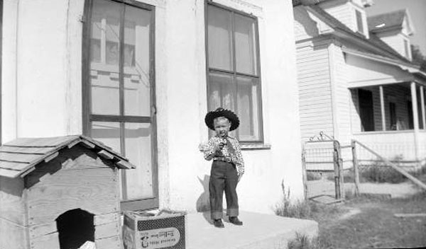 Young boy posing in cowboy attire in front of house (Мальчик, позирующий в наряде ковбоя перед домом), c.1950s