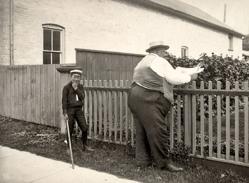 A boy holding a stick contemplates hitting backside of a large man (Мальчик с палкой, раздумывающий над возможностью ударить по заду толстяка)