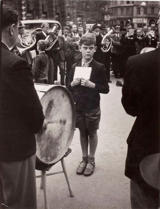 Young man holding sheet of music in front of drum player during public concert (Молодой человек, держащий ноты перед барабанщиком во время общественного концерта), 1948