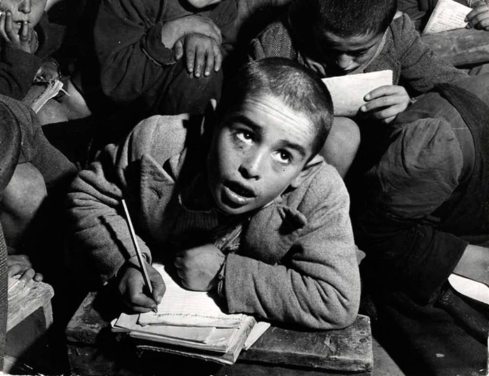 Boy in a classroom, writing on a notebook, and listening with eyes up (Мальчик в классе, пишет на тетради и слушает, глядя вверх), 1948