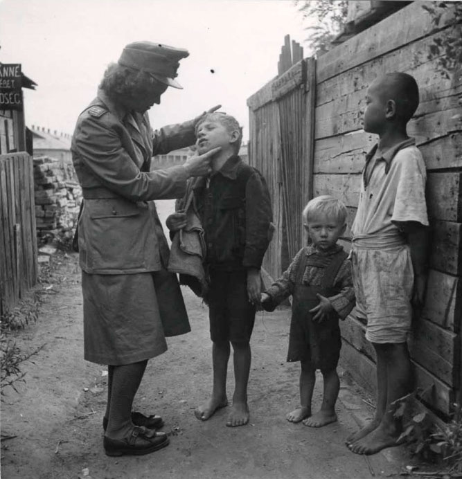 A policewoman looking at the face of a young boy with no shoes (Женщина-полицейский, осматривающая лицо мальчика без обуви), 1948