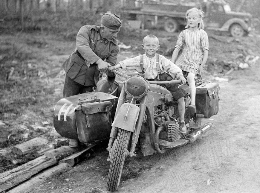 A German soldier showing his BMW R12 motorcycle to local Finnish children somewhere on the Raate Road (Немецкий солдат демонстрирует свой мотоцикл BMW R12 местным финским детям где-то на Раатской дороге), 1941