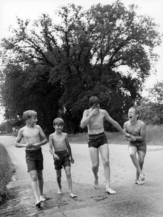 Four boys in swimsuits are laughing and smiling as they walk down a road (Четыре мальчика в купальных костюмах смеются и улыбаются, идя по дороге), before 1979