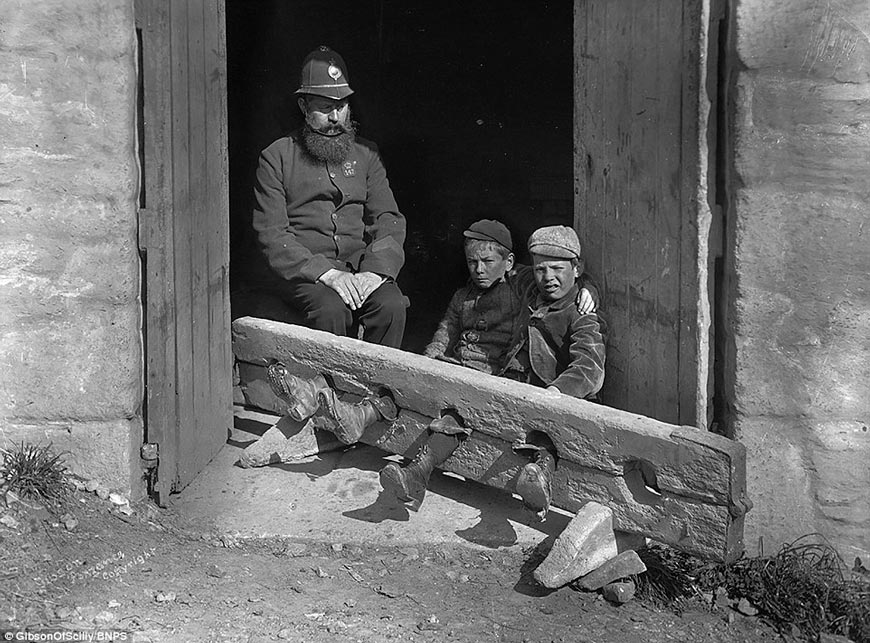 A police officer keeps his eye on two young schoolboys who have been locked up in the stocks (Полицейский следит за двумя школьниками, заковаными в колодки), c.1900