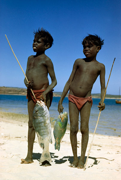 Smiling boys stand on beach with fish they caught with spear (Улыбающиеся мальчики, стоящие на берегу океана с рыбой, пойманной с помощью копий)